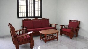 Una habitaci ón con sofá, dos sillas y una mesa de centro de madera, y una ventana con diseño de celosía.