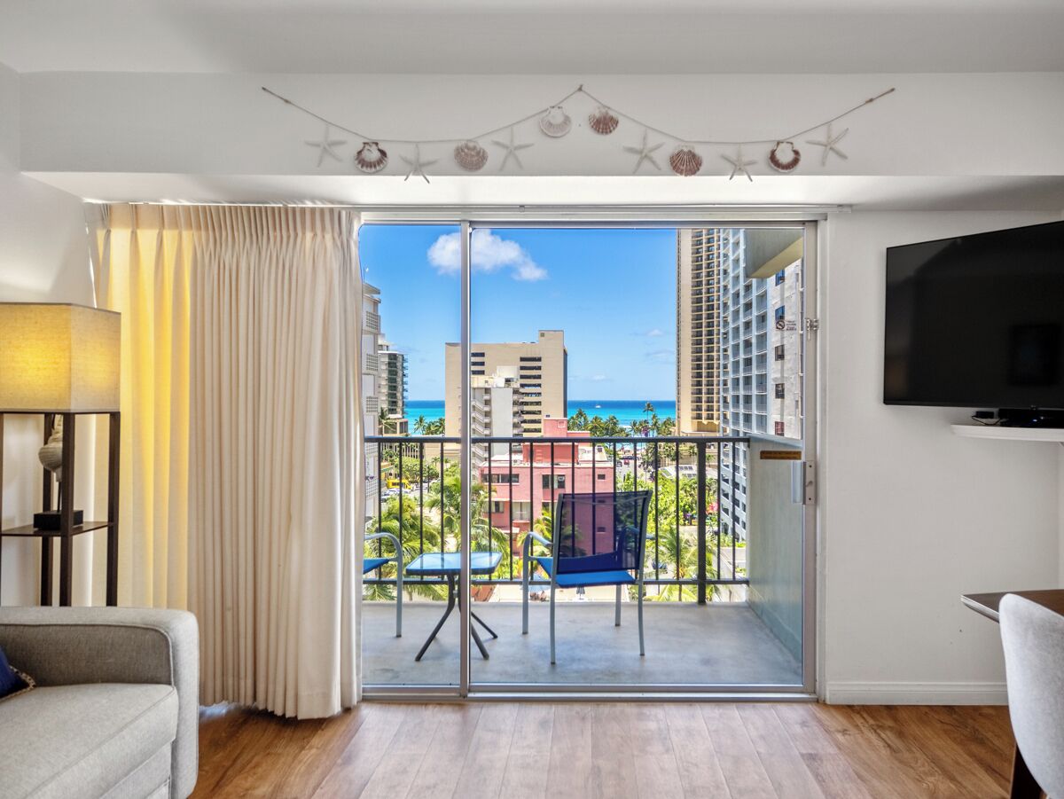 Ein modernes Wohnzimmer mit Balkon, einer Couch, einem Fernseher und Blick auf das Meer und Gebäude.