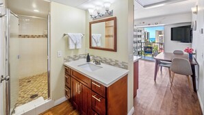 Ein Badezimmer mit Dusche, Waschbecken mit Spiegel und einem Balkon mit Tisch und Stühlen.