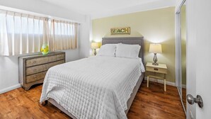 Ein Schlafzimmer mit Bett, Nachttischen, Kommode und einem Fenster mit Vorhängen.