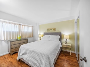 Een slaapkamer met een bed, nachtkastjes, een dressoir en een raam met gordijnen.