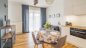 A modern kitchen with a dishwasher, a dining table set for four, and a large window with curtains. - Rakowicka Apt - Main Station, Old Town nearby - by Rentujemy (Kraków)