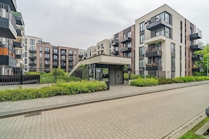 Ein modernes Mehrfamilienhaus mit mehreren Balkonen, einem überdachten Eingangsbereich und einem gepflasterten Weg.
