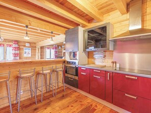 A kitchen with wooden beams, a bar area with stools, and stainless steel appliances.