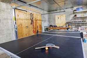 A ping pong table with a ball and paddles, a wooden door, and a workbench with tools.