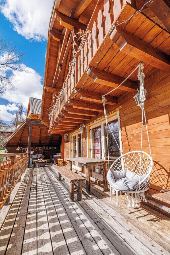 Une terrasse en bois avec une chaise suspendue, une table et un banc.