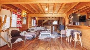 A wooden cabin interior with a living area, sofa, coffee table, and a kitchen area with a TV.