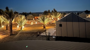 Un campement dans le désert, de nuit, avec des tentes, des palmiers et une lune brillante.