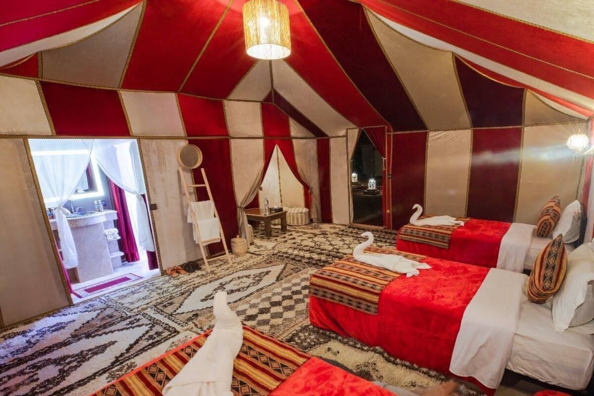 A tent-style room with multiple beds, a chandelier, and a patterned carpet.