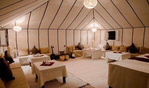 A tented accommodation with multiple beds, tables, and a television. - nomadcampmerzouga (Merzouga)