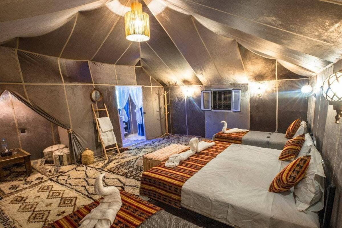 A tented room with two beds, a ladder, a small table, and a hanging light fixture.