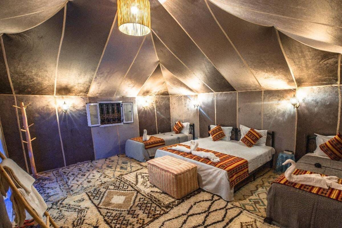 A tent-style room with three beds, a patterned rug, and wall-mounted lights.
