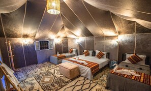 A tent-style room with three beds, a patterned rug, and wall-mounted lights. - nomadcampmerzouga (Merzouga)