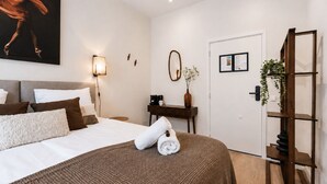 A hotel room with a bed, a desk, a mirror, and a door.