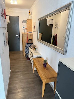 Ein Flur mit einer Holzbank, einem Spiegel, einem kleinen Tisch mit einer Pflanze und einem Kleiderhaken mit Kleidung.