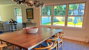 Un comedor con una mesa y sillas de madera, una cesta tejida y ventanas amplias con vistas al exterior.