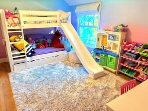A bunk bed with a slide, a play kitchen, and a toy storage unit in a child's room.