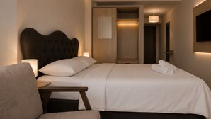 Una camera d'albergo con un letto, un comodino, una sedia e una TV montata a parete.