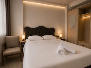 A neatly made bed with a rolled towel, a chair, bedside lamps, and a wardrobe. - Kadıkoy Metro Central Apart  (İstanbul)
