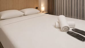 Una camera d'hotel con un letto, un comodino, una lampada, un asciugamano e una finestra con tende.