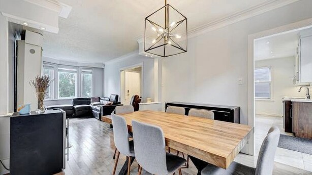 Un espace repas moderne avec une table et des chaises en bois, un luminaire suspendu aux formes géométriques, et une vue sur la cuisine et le salon.