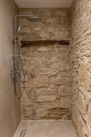 A stone-walled shower enclosure with a handheld showerhead and a wall-mounted faucet.