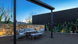 An outdoor patio with a stone wall, a metal pergola, and a seating area with cushions.