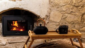 A stone fireplace with a visible fire, a wooden tray with a teapot and cup, and a cozy blanket.