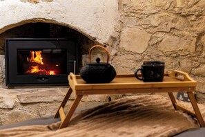 A stone fireplace with a visible fire, a wooden tray with a teapot and cup, and a cozy blanket.