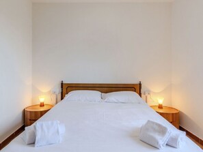 A neatly made bed with white linens and two bedside tables with lamps.