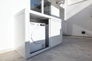 Ein kompakter, moderner Waschraum mit integriertem Waschmaschine und Trockner, großen Fenstern und Fliesenboden.