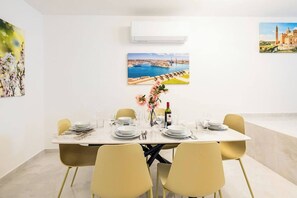 Ein Esszimmer mit einem weißen Tisch, gedeckt für sechs Personen, gelben Stühlen und Bildern an den Wänden.