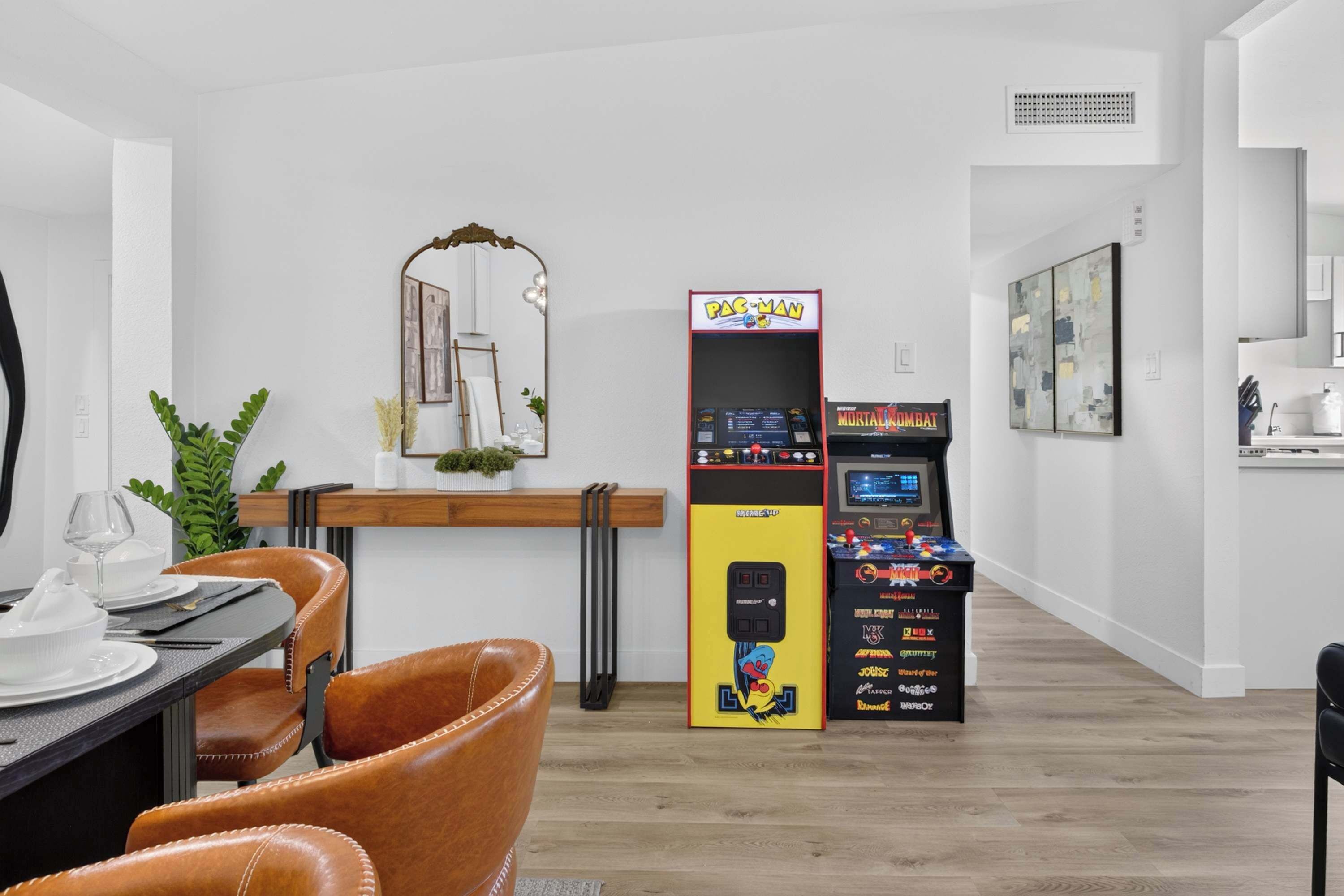Una sala de estar moderna con comedor, una máquina de Pac-Man y una máquina de Mortal Kombat.