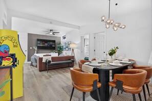 A modern living room with a sofa, dining table, and chairs. There is a television mounted on the wall and a ceiling fan. - 8BR Power Stay | Space, Comfort & Modern Living! (North Las Vegas)