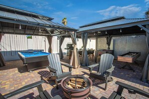 An outdoor patio with a pool table, two Adirondack chairs, a fire pit, and a foosball table. - 8BR Power Stay | Space, Comfort & Modern Living! (North Las Vegas)