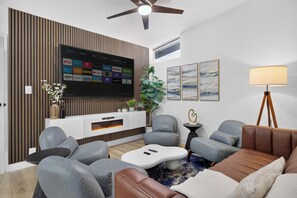 Ein modernes Wohnzimmer mit Flachbildfernseher, grauen Sofas, einem Couchtisch und einem Deckenventilator.