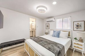Ein Schlafzimmer mit Bett, Nachttisch, Bank und einem durchgegangenen Türspalt sichtbarem Badezimmer.