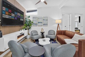 A modern living room with a flat-screen TV mounted on the wall, grey sofas, a brown leather couch, a small round table, and a floor lamp. - 8BR Power Stay | Space, Comfort & Modern Living! (North Las Vegas)