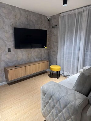 En moderne stue med et fladskærms-tv monteret på væggen, et trækonsolbord, en gul stol og en grå sofa.