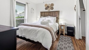 Une chambre à coucher comprenant un lit, un ventilateur de plafond, une table de chevet, une lampe, un objet décoratif fixé au mur et un panier à linge.