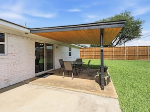 A patio with a table and chairs, a covered area, and a wooden fence in the background. - Santa Clara | Large Backyard+ 2 Queen Beds (Frisco)