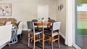 Un coin repas doté d’un ventilateur de plafond, d’une table à manger avec des chaises, d’une porte et d’une vue sur le jardin à travers une porte-fenêtre coulissante.