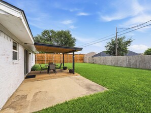A backyard with a covered patio, a wooden fence, and a grassy lawn. - Santa Clara | Large Backyard+ 2 Queen Beds (Frisco)