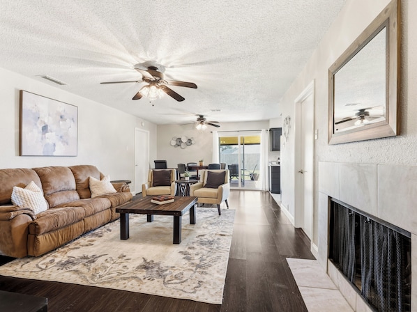 A modern living room with a brown leather sofa, a coffee table, and a fireplace. - Santa Clara | Large Backyard+ 2 Queen Beds (Frisco)