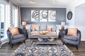 Uma sala de estar com um sofá, duas poltronas, uma mesa de centro e um tapete estampado.
