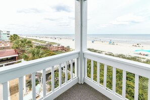 Un balcon donnant sur une plage, une piscine et un bâtiment doté d’une balustrade blanche.