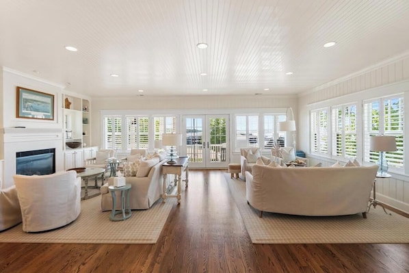 A spacious living room with a fireplace, white furniture, and large windows. - Harbor Cottage: 4  BR, 3.5  BA Cottage in Harbor Springs , Sleeps 12 (Harbor Springs)