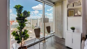 A modern room with large windows, a potted plant, two chairs, a cabinet, and a city view. - Boulevard Stays Highrise STU Sky Pool, Gym 38 (Phoenix)