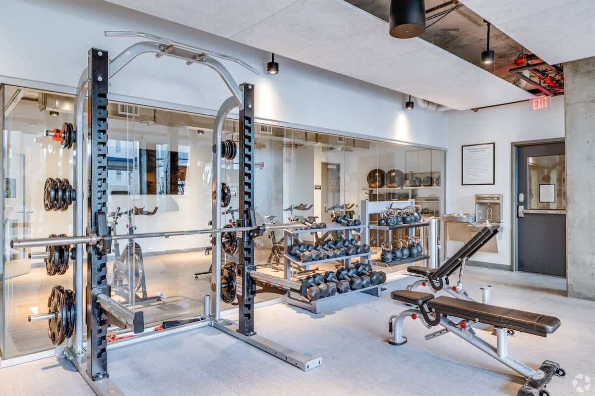 A modern gym with weightlifting equipment, benches, and a mirrored wall.