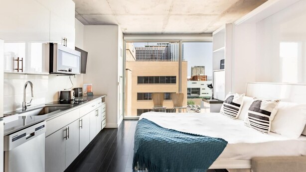 A modern hotel room with a kitchen, a bed with a blue throw, and a view of the city. - Boulevard Stays Highrise STU Sky Pool, Parking, Gym 35 (Phoenix)